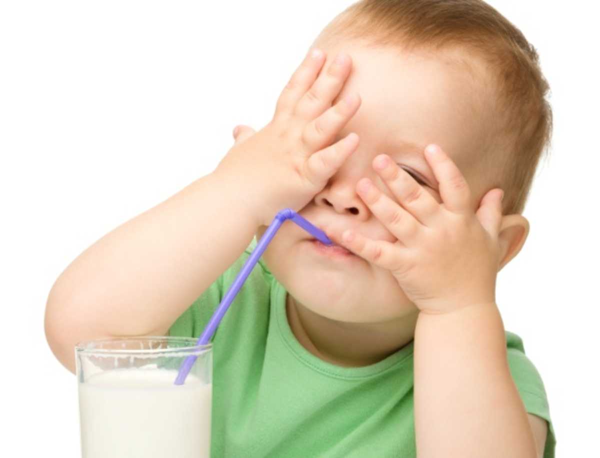 Criança com as mãos no rosto ingere pelo canudo líquido branco contido em copo