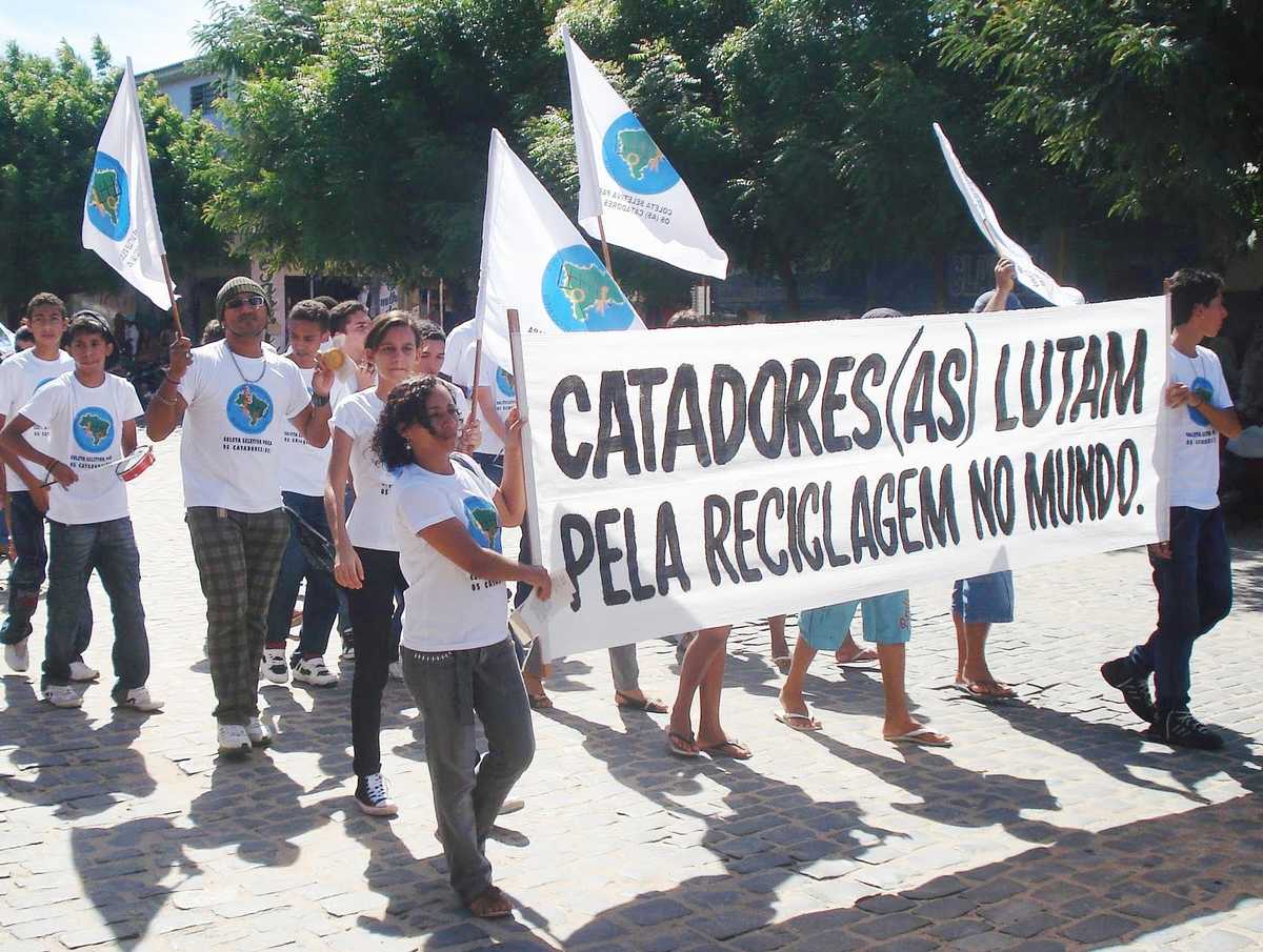 Pessoas com bandeirolas, camisetas e faixa onde se lê: 