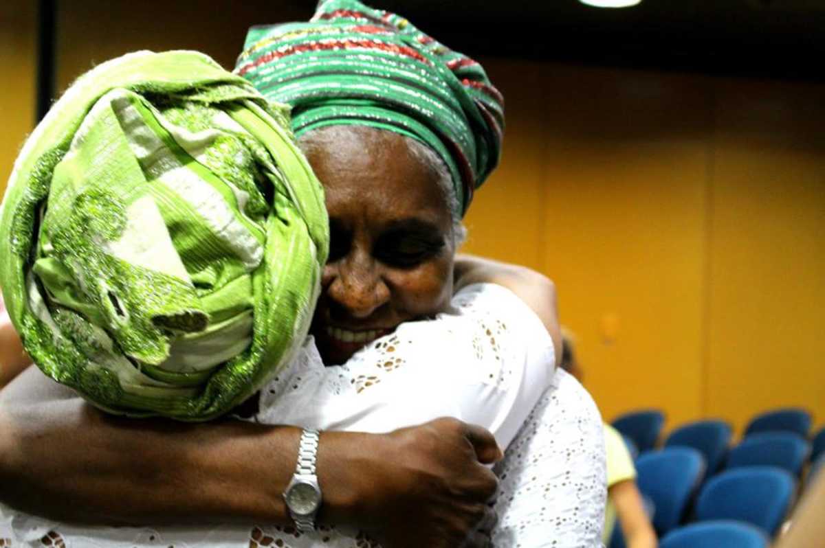 Duas mulheres negras, com turbantes na cabeça, se abraçam