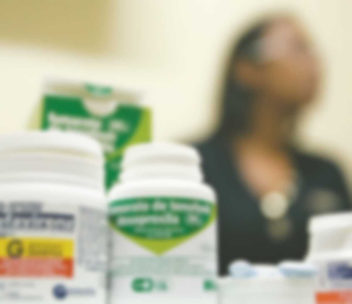 Embalagens de medicamentos em primeiro plano e paciente ao fundo com a imagem desfocada