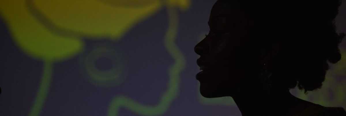 Silhueta de rosto de mulher negra com desenho ao fundo de rosto de mulher negra