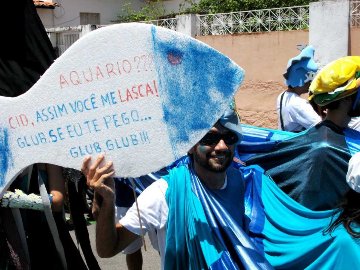 Folião com fantasia nas cores azul e branco ironiza obra do Governo do Estado carregando isopor em formato de peixe com os dizeres: Aquário? Cid, assim você me lasca! Glub se eu te pego... Glub, glub