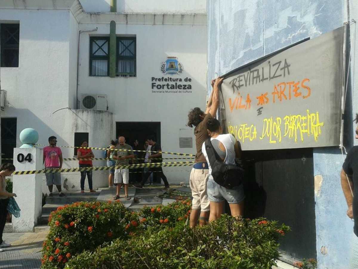 Pessoas erguem faixa reivindicando reabertura da Biblioteca Dolor Barreira e a finalização do projeto Vila das Artes