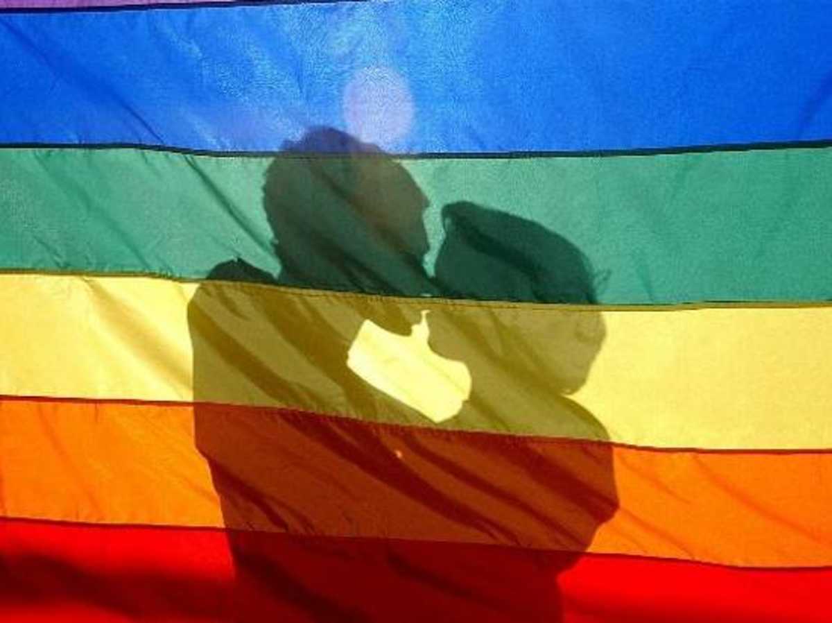 Sombra de duas pessoas se beijando atrás de uma bandeira com as cores do arco-íris