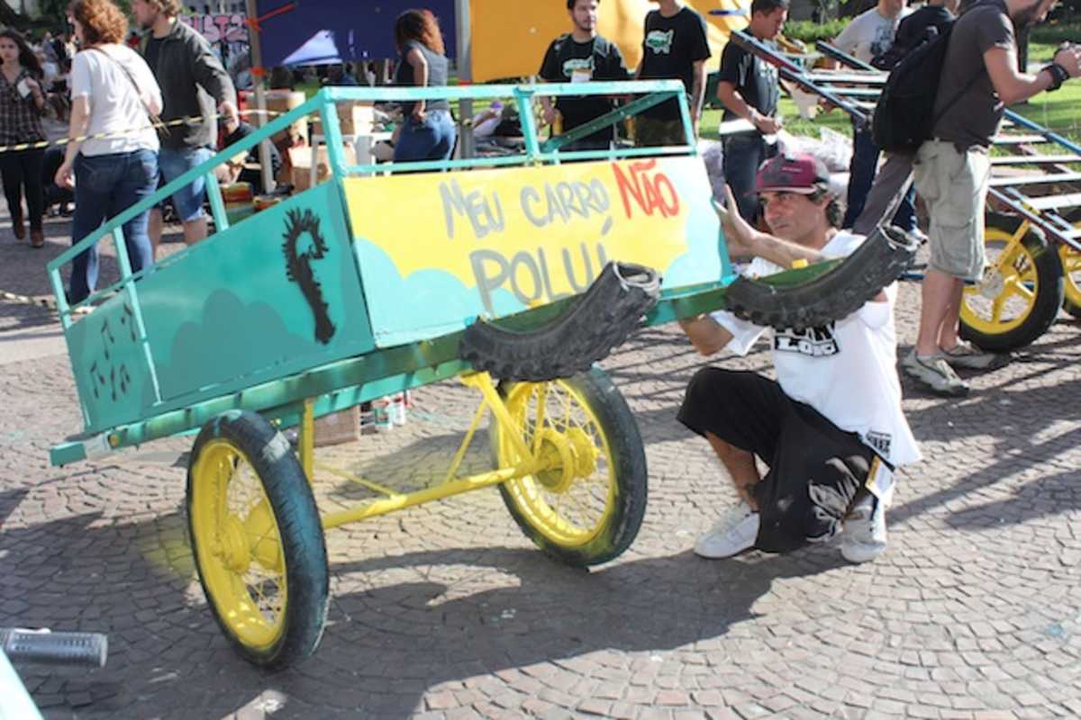Pessoa ajusta carrinho utilizado por catador de materiais recicláveis pintado em verde e amarelo com dizeres em cinza e vermelho: 